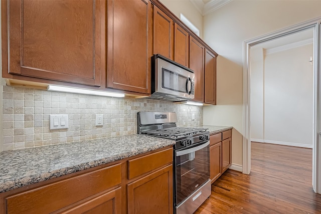 5938 Kansas St, Houston, TX 77007 - kitchen featuring appliances with stainless steel finishes, crown molding, wood finished floors, brown cabinets, and dark stone counters