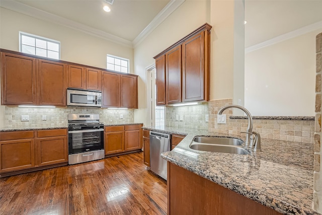 5938 Kansas St, Houston, TX 77007 - kitchen featuring stainless steel appliances, a sink, brown cabinets, light stone counters, and ornamental molding