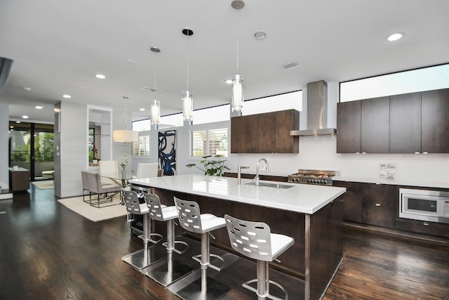 kitchen featuring dark wood-style flooring, light countertops, wall chimney range hood, and a sink