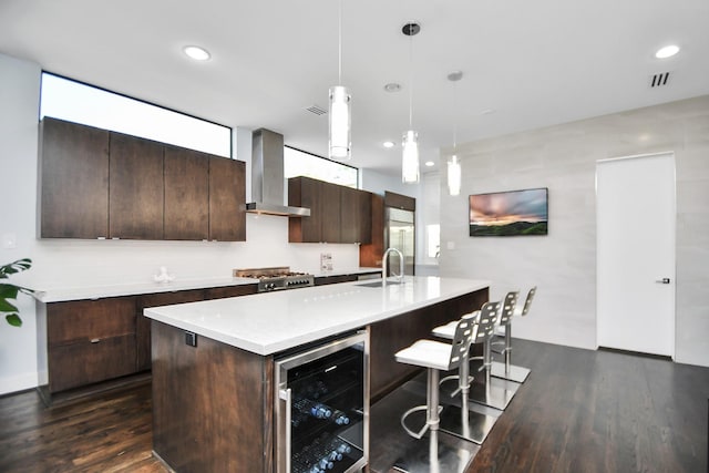 kitchen with beverage cooler, a sink, wall chimney range hood, dark brown cabinetry, and light countertops