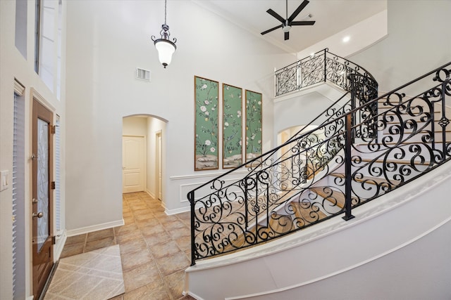 stairway with visible vents, baseboards, a towering ceiling, arched walkways, and a ceiling fan