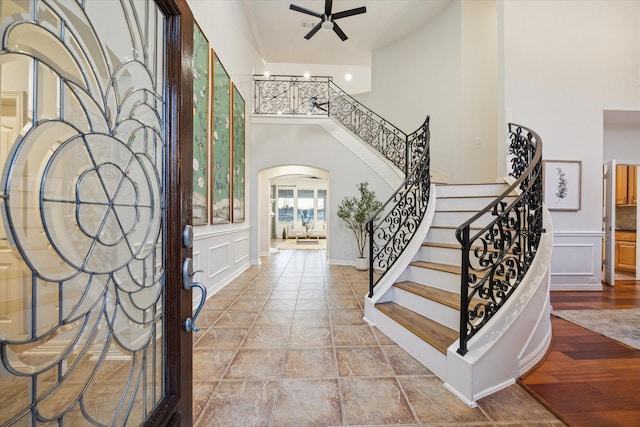 foyer with arched walkways, a decorative wall, stairs, and ceiling fan