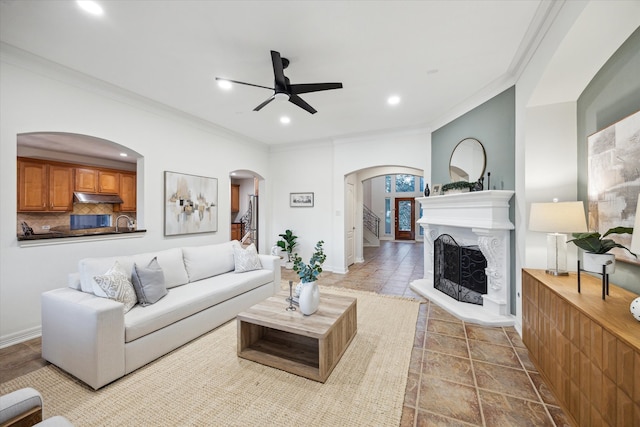 living area featuring recessed lighting, a fireplace with raised hearth, arched walkways, ceiling fan, and crown molding