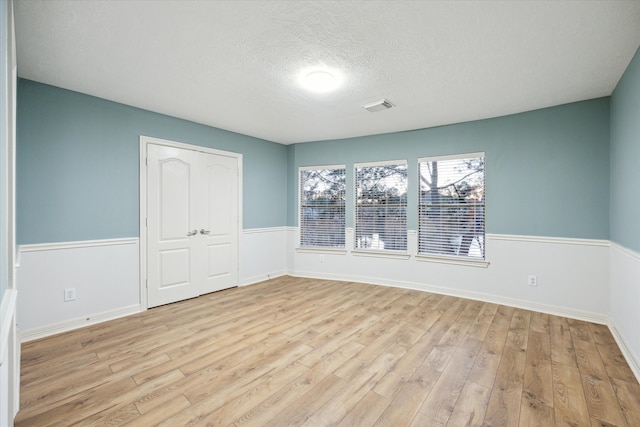 unfurnished room featuring a textured ceiling, wainscoting, visible vents, and light wood-type flooring