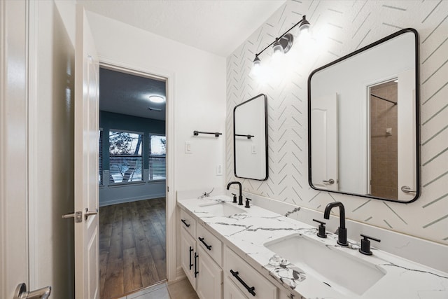 bathroom featuring double vanity, wallpapered walls, a textured ceiling, and a sink