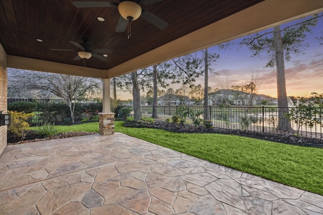 patio terrace at dusk featuring a yard, a fenced backyard, and a ceiling fan