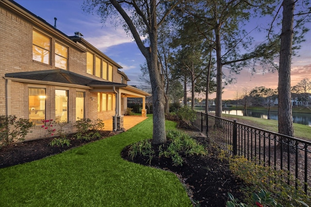 yard at dusk featuring fence and a water view