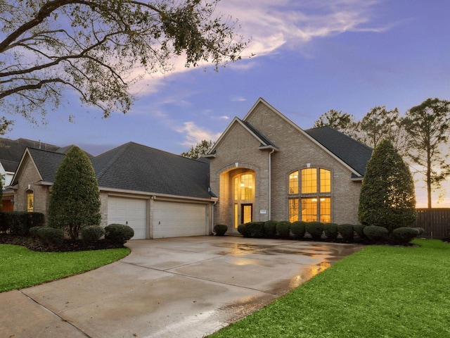 view of front of property featuring roof with shingles, an attached garage, a yard, concrete driveway, and brick siding