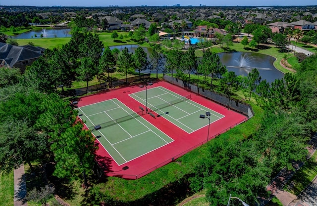 view of tennis court featuring fence, a water view, and a residential view