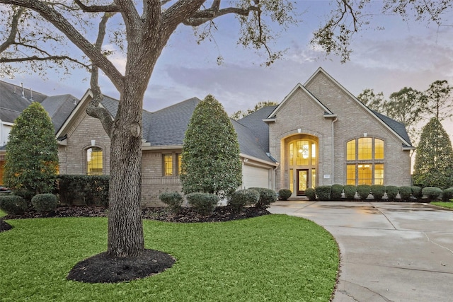 view of front facade with brick siding, a yard, concrete driveway, and a garage