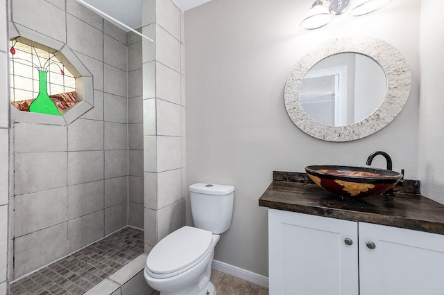 full bathroom featuring baseboards, tiled shower, vanity, and toilet