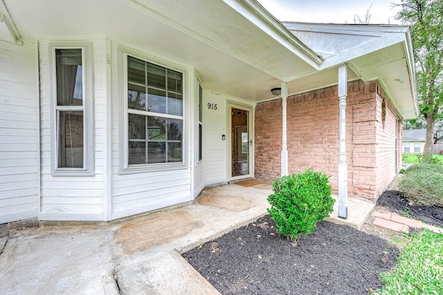 view of exterior entry with a porch and brick siding