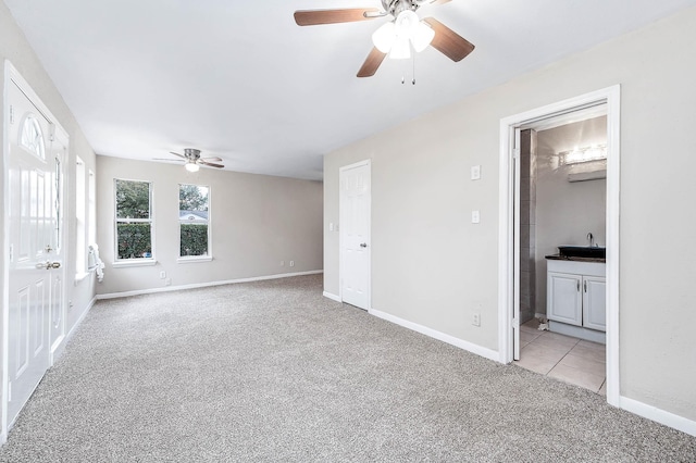 unfurnished bedroom with light colored carpet, ceiling fan, ensuite bath, and baseboards