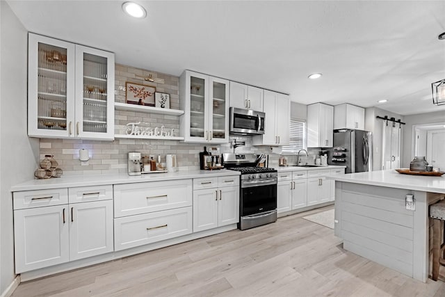 kitchen with light wood finished floors, a sink, stainless steel appliances, white cabinetry, and backsplash