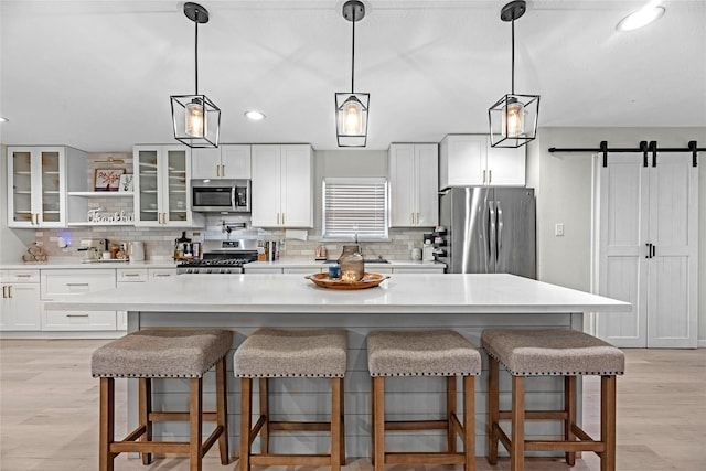 kitchen with a barn door, a kitchen island, stainless steel appliances, light wood-type flooring, and white cabinetry