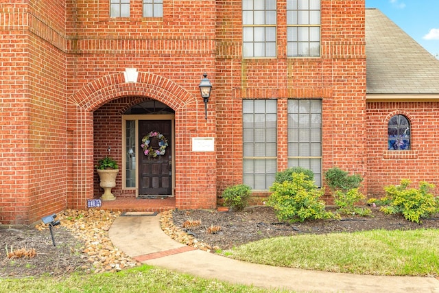 property entrance with a shingled roof and brick siding