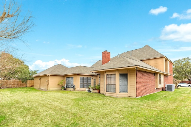 back of property with cooling unit, brick siding, fence, a yard, and a chimney