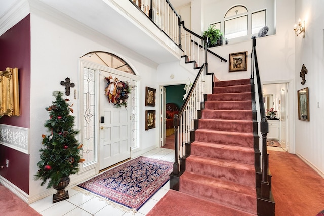 tiled foyer with stairs, a high ceiling, and baseboards