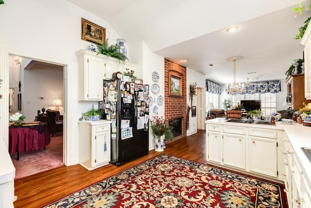 kitchen featuring dark wood finished floors, a peninsula, vaulted ceiling, light countertops, and black fridge