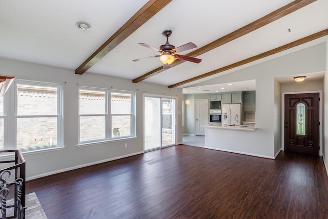 unfurnished living room featuring dark wood finished floors, vaulted ceiling with beams, a ceiling fan, a sink, and baseboards