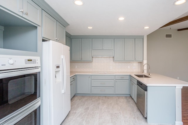 kitchen featuring decorative backsplash, gray cabinetry, a sink, white appliances, and a peninsula