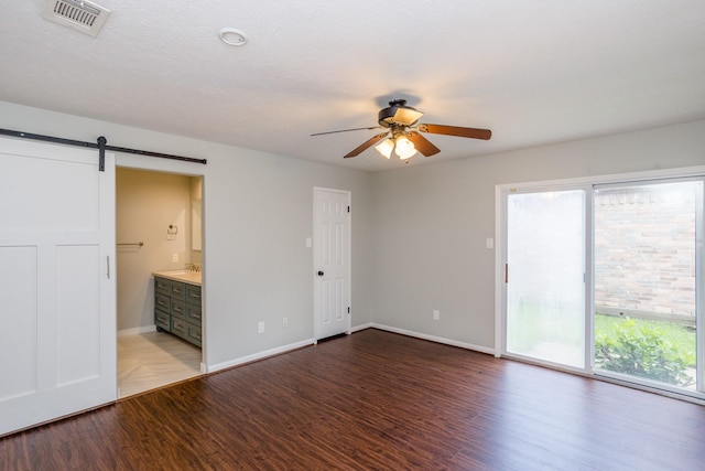 unfurnished bedroom featuring a barn door, wood finished floors, visible vents, baseboards, and access to exterior