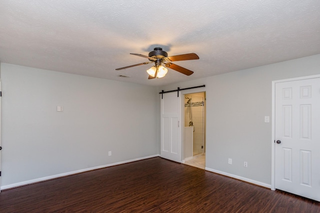 empty room with a ceiling fan, wood finished floors, visible vents, and a barn door