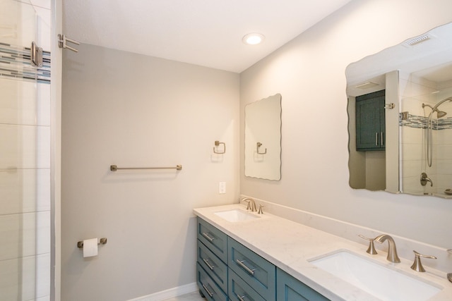 full bath featuring a tile shower, double vanity, a sink, and baseboards