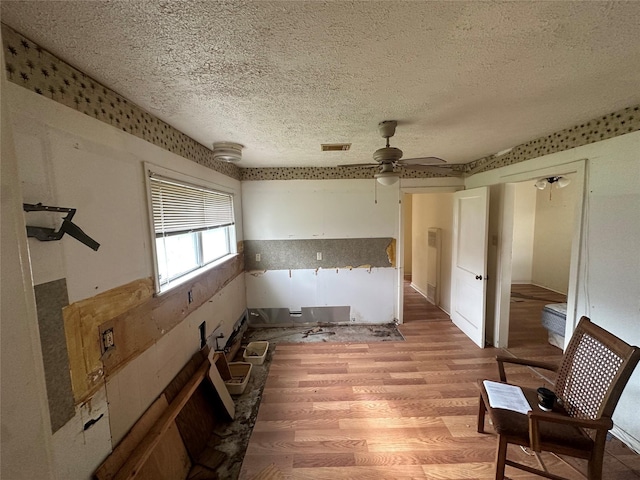 empty room featuring light wood-type flooring, a ceiling fan, visible vents, and a textured ceiling