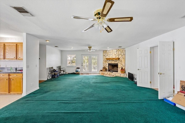 unfurnished living room with a stone fireplace, a ceiling fan, visible vents, and baseboards