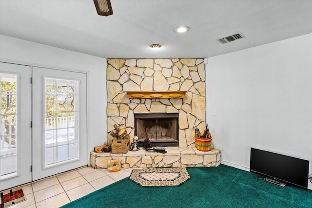 living room featuring a stone fireplace, visible vents, and tile patterned floors