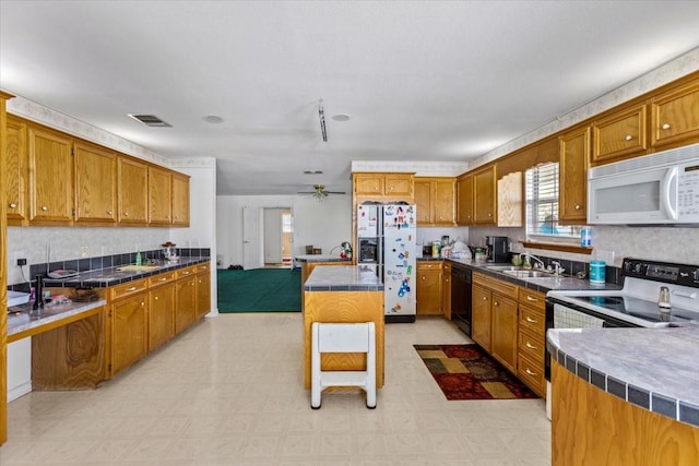 kitchen featuring white appliances, a sink, visible vents, light floors, and brown cabinetry