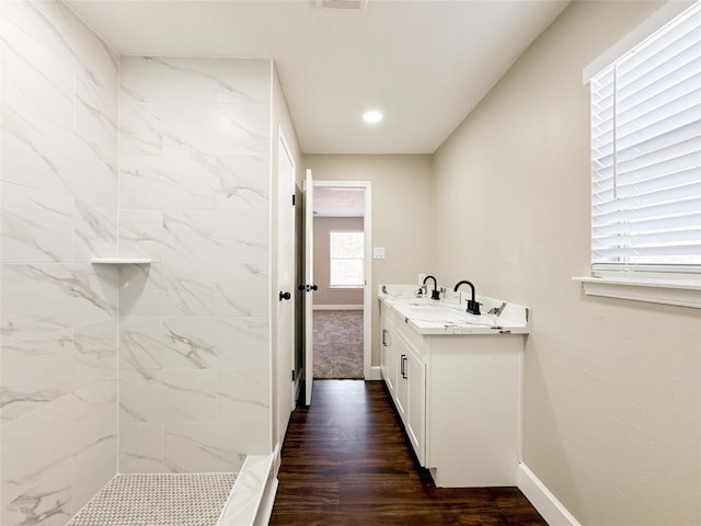 full bathroom with wood finished floors, a tile shower, vanity, and baseboards