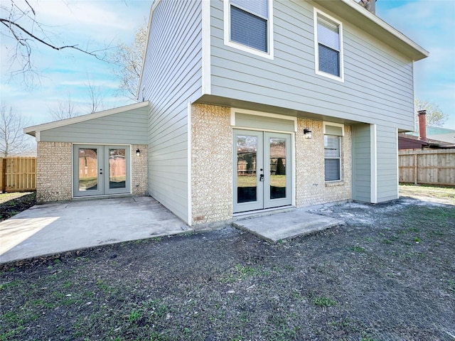 rear view of house with brick siding, a patio area, fence, and french doors