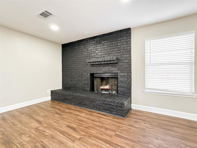 unfurnished living room featuring a brick fireplace, visible vents, baseboards, and wood finished floors