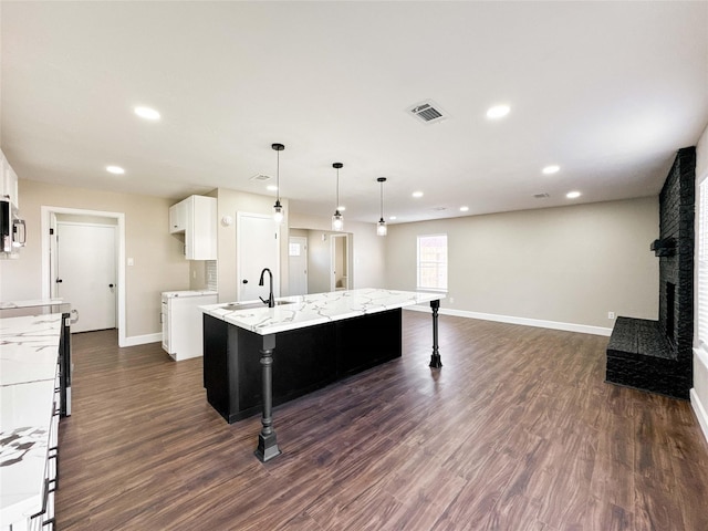 kitchen featuring a kitchen island with sink, a fireplace, white cabinetry, baseboards, and dark wood finished floors