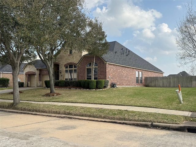 view of front of property featuring brick siding, fence, a garage, driveway, and a front lawn