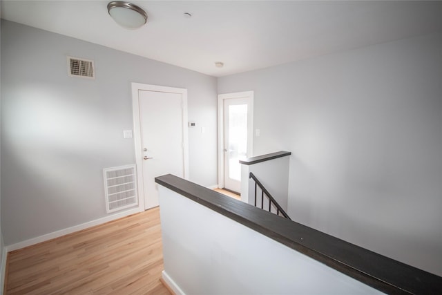 corridor featuring visible vents, an upstairs landing, baseboards, and light wood finished floors