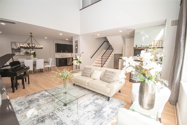 living room featuring stairs, a notable chandelier, wood finished floors, and visible vents