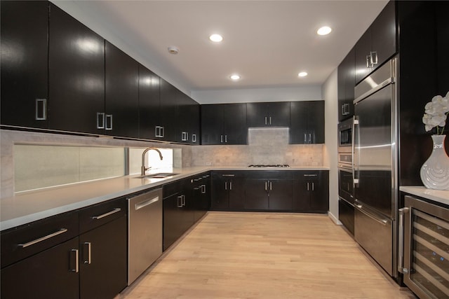 kitchen with beverage cooler, a sink, dark cabinetry, stainless steel appliances, and light countertops