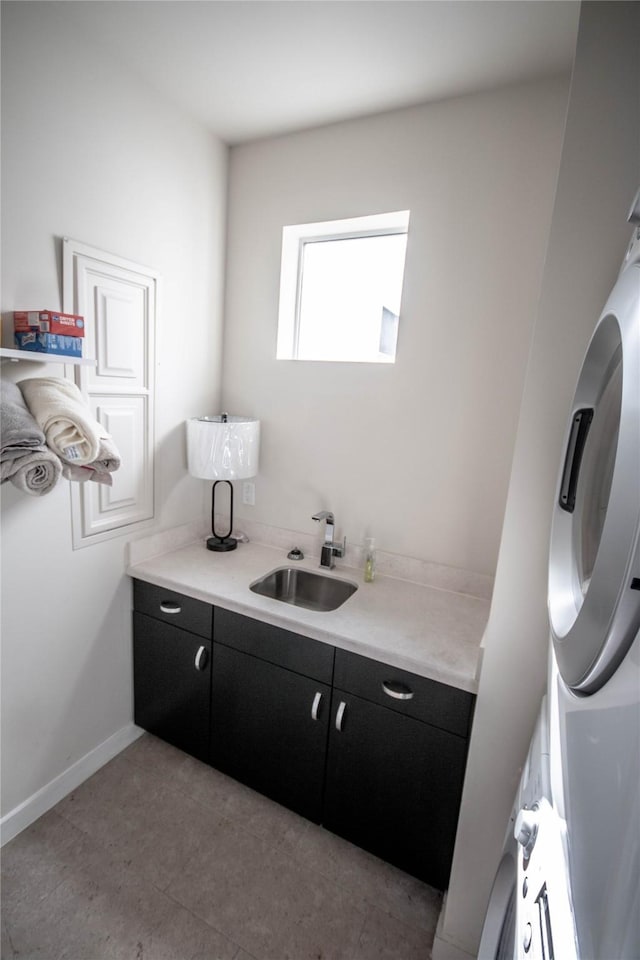 laundry room with baseboards, stacked washer and dryer, light tile patterned floors, cabinet space, and a sink