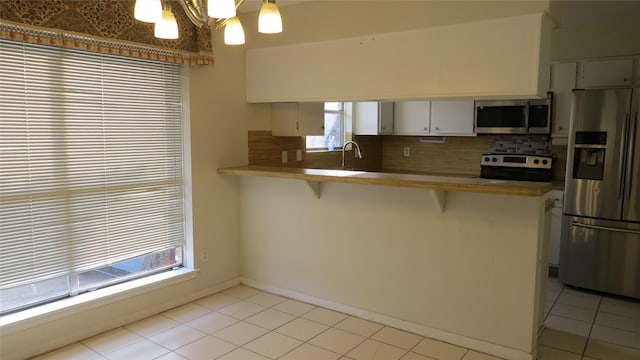 kitchen with a notable chandelier, a breakfast bar area, stainless steel appliances, tasteful backsplash, and a peninsula