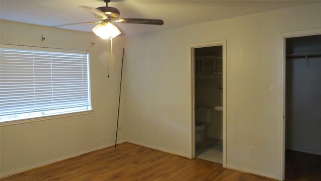 unfurnished bedroom featuring a closet, ceiling fan, ensuite bath, wood finished floors, and baseboards