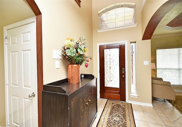 entrance foyer with crown molding, light tile patterned flooring, baseboards, and arched walkways