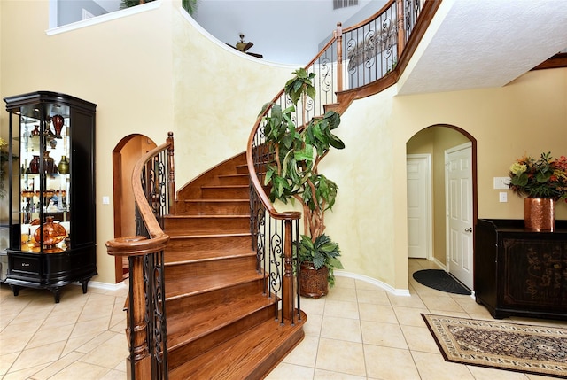 stairs featuring baseboards, arched walkways, a high ceiling, and tile patterned flooring