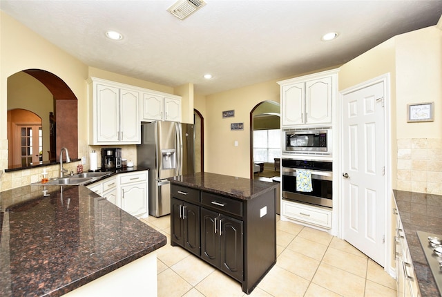 kitchen with a sink, white cabinetry, arched walkways, appliances with stainless steel finishes, and light tile patterned floors