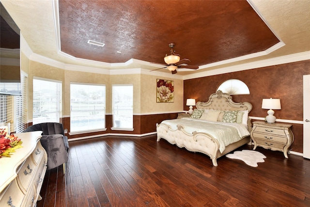 bedroom with visible vents, a tray ceiling, ornamental molding, wainscoting, and wood-type flooring