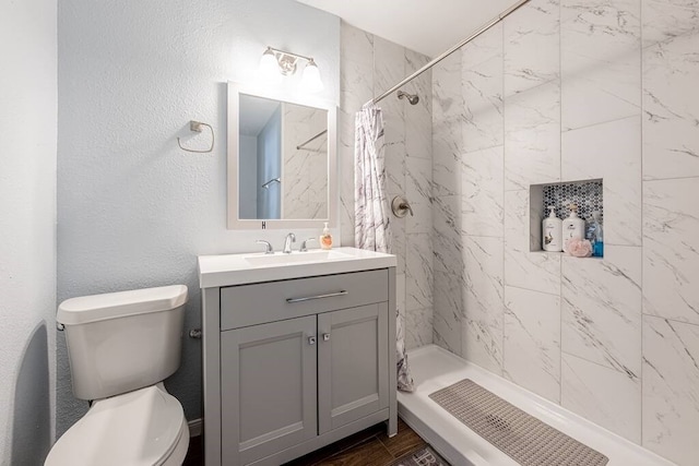 full bathroom with toilet, a stall shower, a textured wall, and vanity