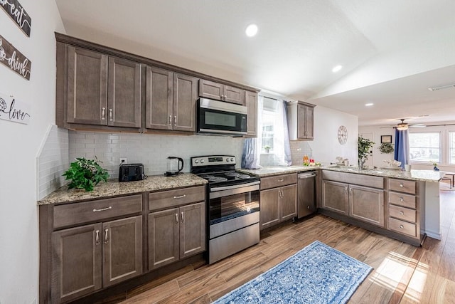 kitchen featuring visible vents, appliances with stainless steel finishes, a peninsula, vaulted ceiling, and light wood-type flooring