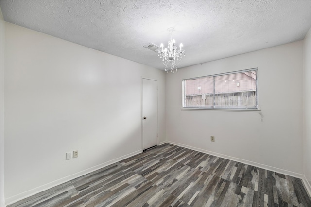 empty room with a textured ceiling, a notable chandelier, wood finished floors, visible vents, and baseboards